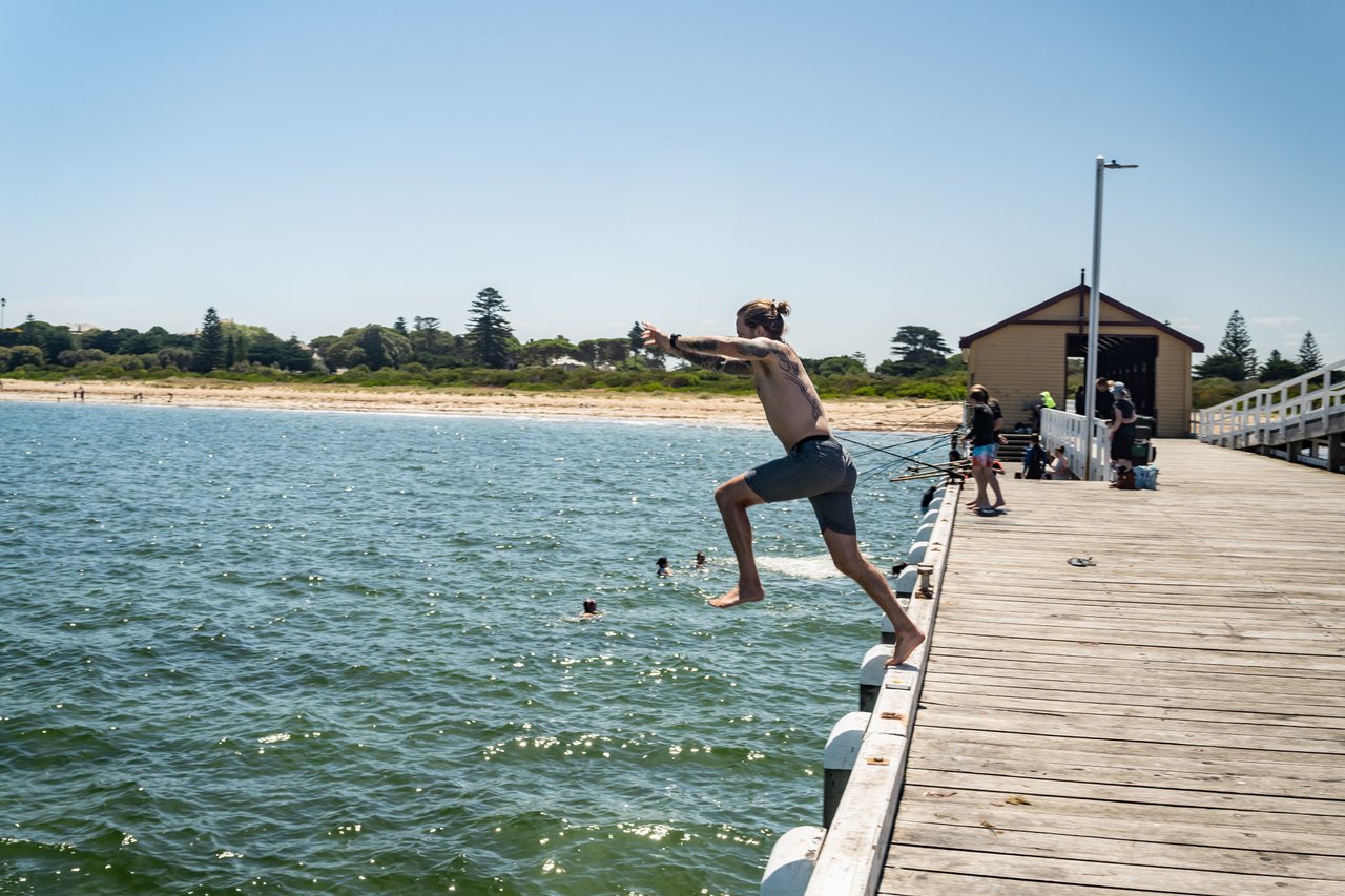 A man in board shorts jumping off a pier into the ocean. 
