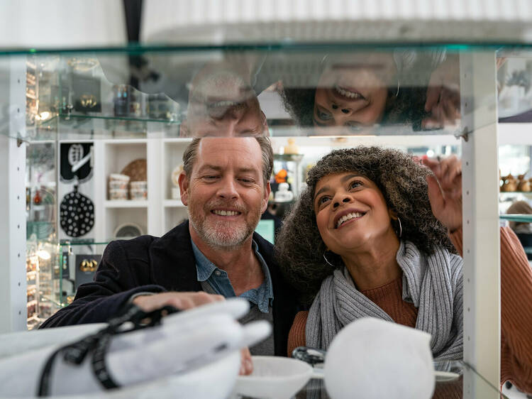 A man and a woman smile looking through a shelf of retail items to purchase.