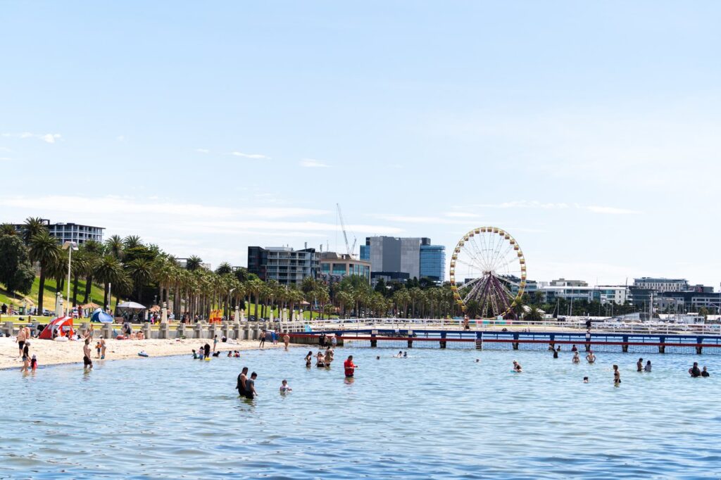 People swimming in promenade at Eastern Beach. The Ferris Wheel is in the background, skies are blue.